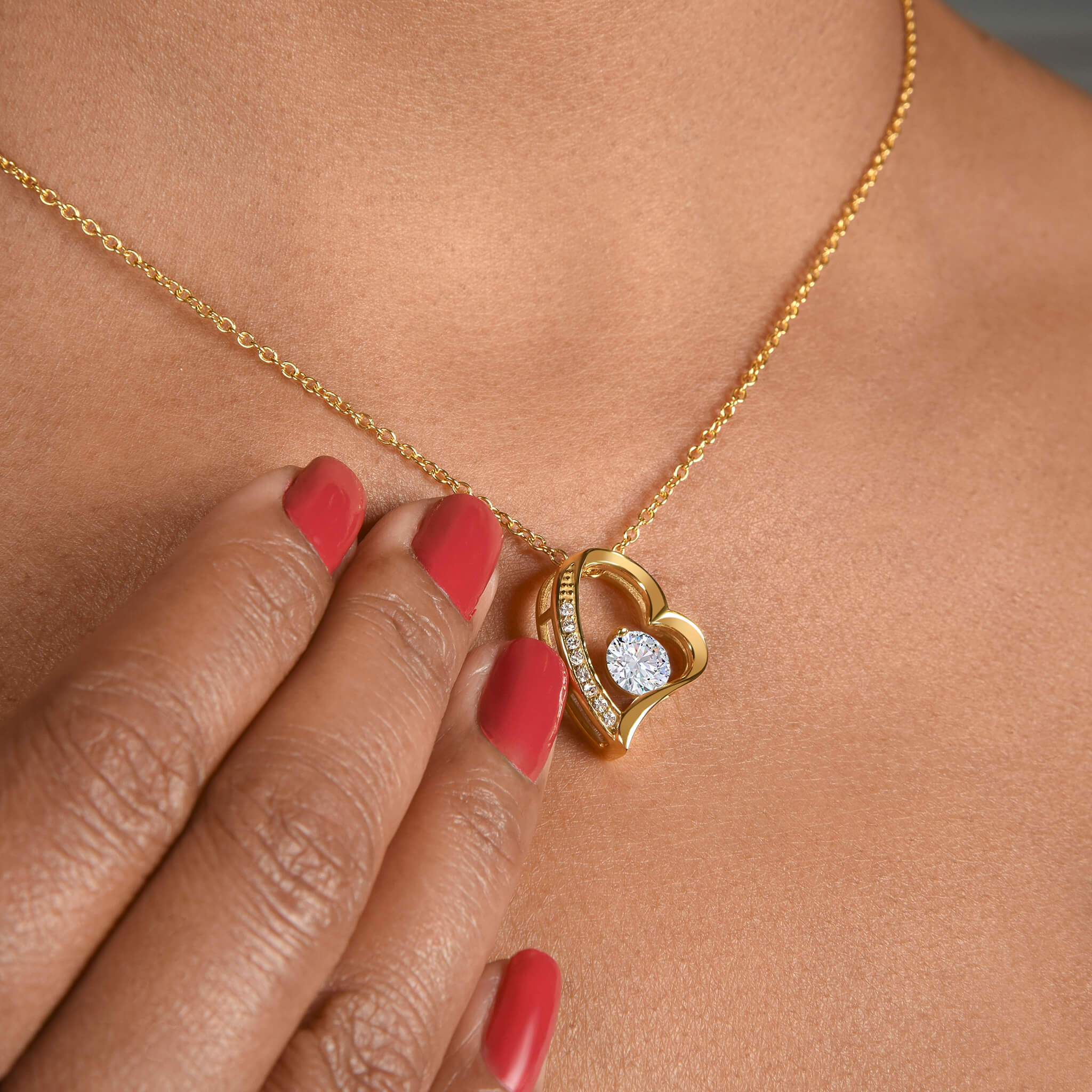 Closeup of model wearing the Passion necklace in 18k gold finish with her fingertips resting on her chest next to the heart-shaped pendant, highlighting its dainty size.